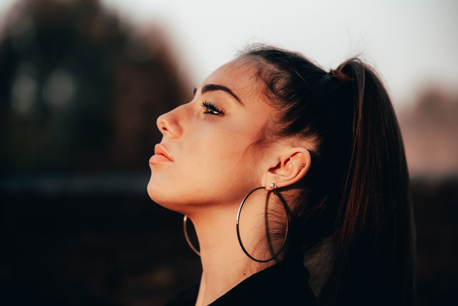 Mujer joven de perfil con coleta y aro grande dejando ver la oreja